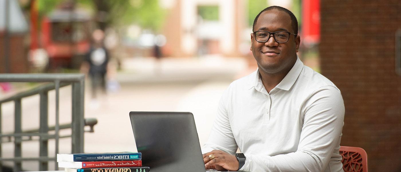 Criminal justice student sitting at an outdoor table on campus using his laptop